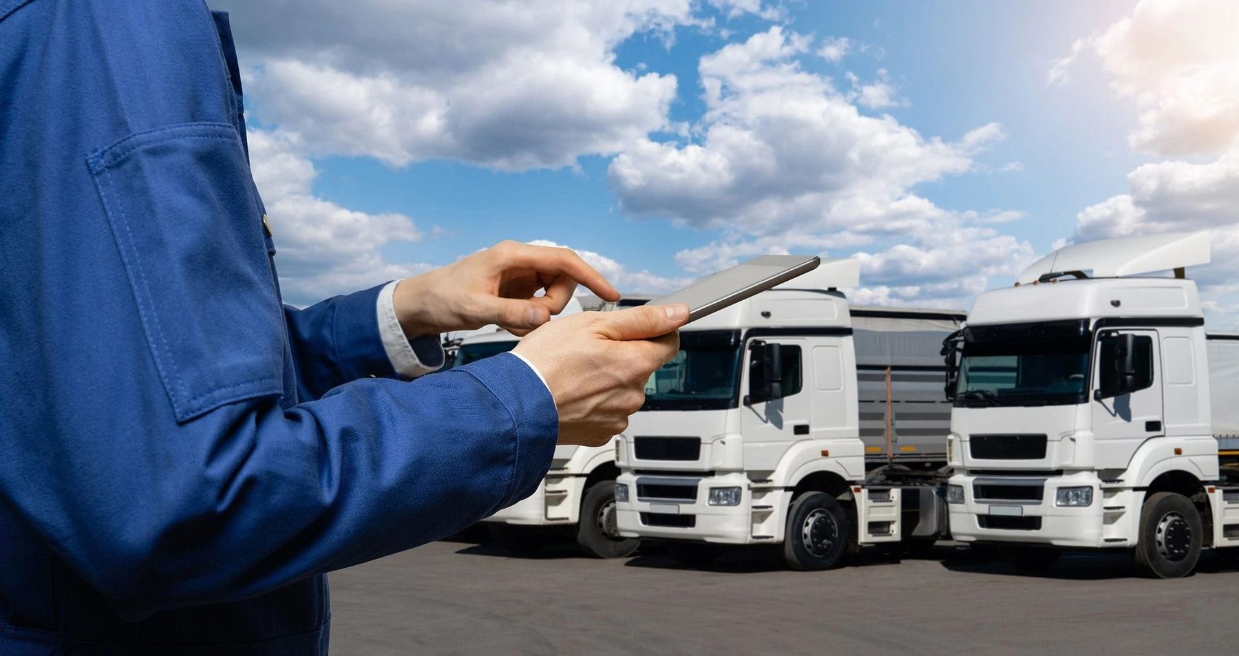 A technician with a tablet checking a pair of parked fleet trucks