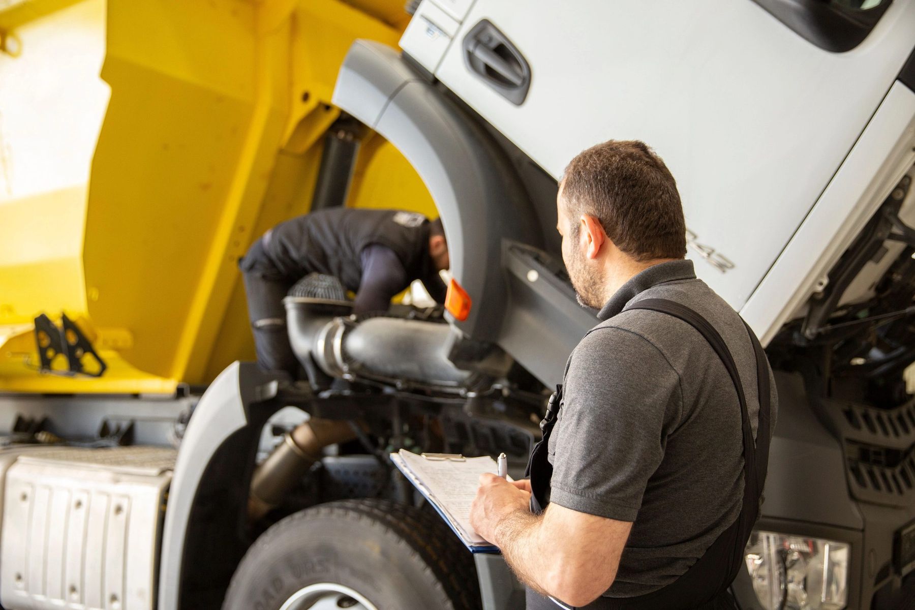 Two technicians working under the raised bonnet of a truck